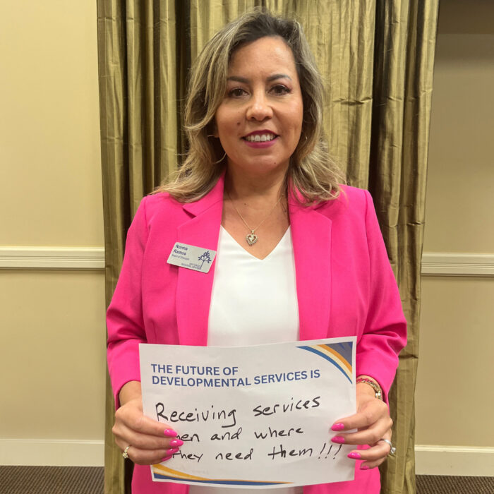Norma Ramos smiles at the camera while holding a sign that reads: "The future of developmental services is receiving services when and where they need them!!!"